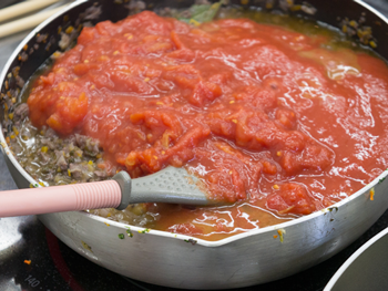 汁気が無くなったら、手でつぶしたトマトの水煮を缶汁事加え、煮込んで水煮トマトの水分をとばします